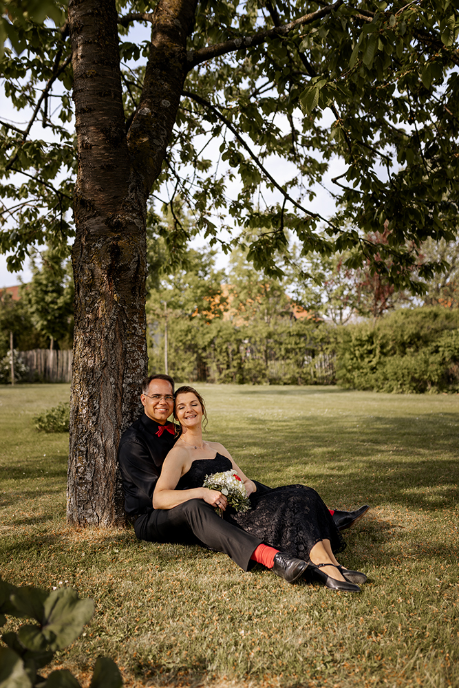 Das Hochzeitspaar sitzt unter einem Baum. Er hält sie im Arm